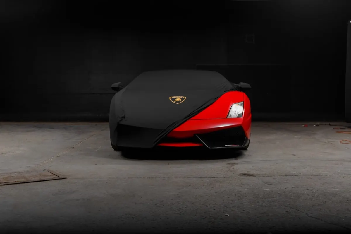 A red Lamborghini Gallardo half-revealed beneath a black car cover in a private garage